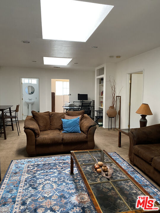 Living room at 2643 S Spaulding Avenue with brown sofas, a blue patterned rug, and a glass coffee table, opening to a dining area and kitchen.