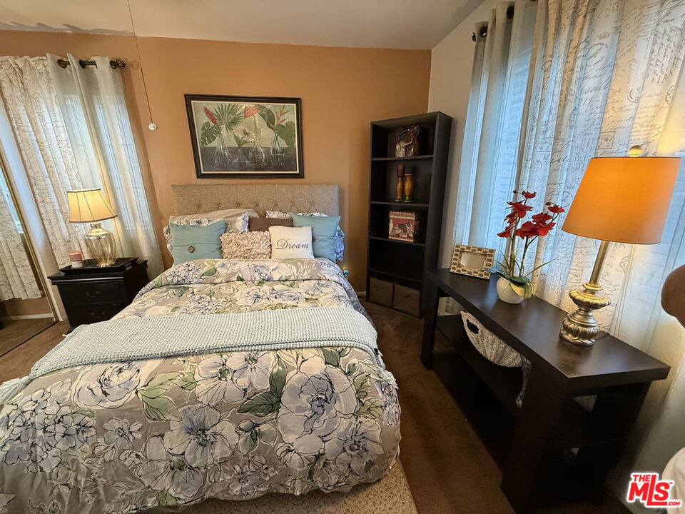Bedroom at 2643 S Spaulding Avenue with a queen bed, floral bedding, matching nightstand, bookcase, and a dark desk beneath curtained windows.