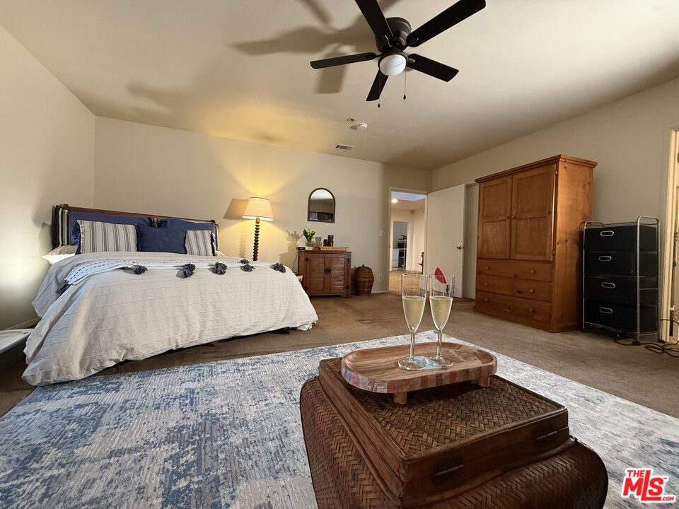 Spacious bedroom at 2643 S Spaulding Avenue with a king-size bed, blue area rug, wooden wardrobe, ceiling fan, and champagne glasses on a coffee table.