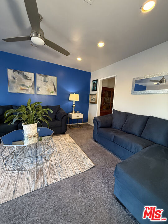 Living room at 2643 S Spaulding Avenue with blue walls, navy sofas, a glass coffee table, and a ceiling fan.