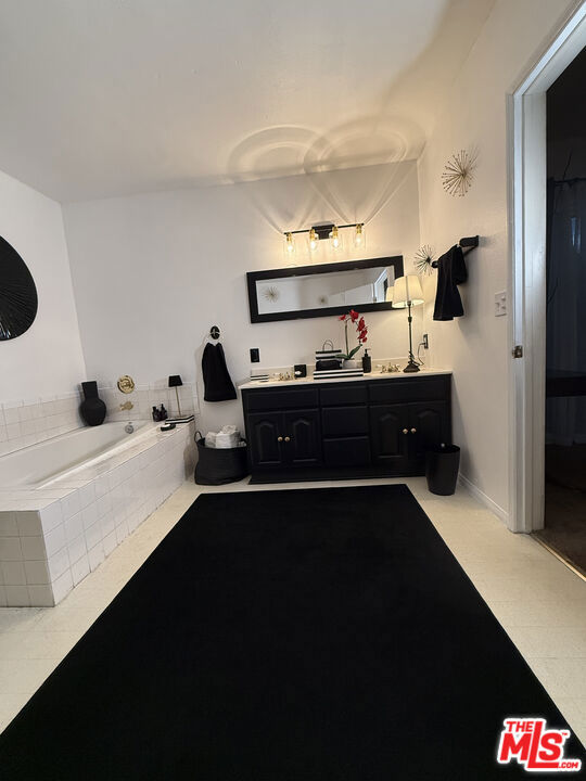 Bathroom at 2643 S Spaulding Avenue with a white tiled soaking tub, black vanity, wide mirror, and long black floor rug.