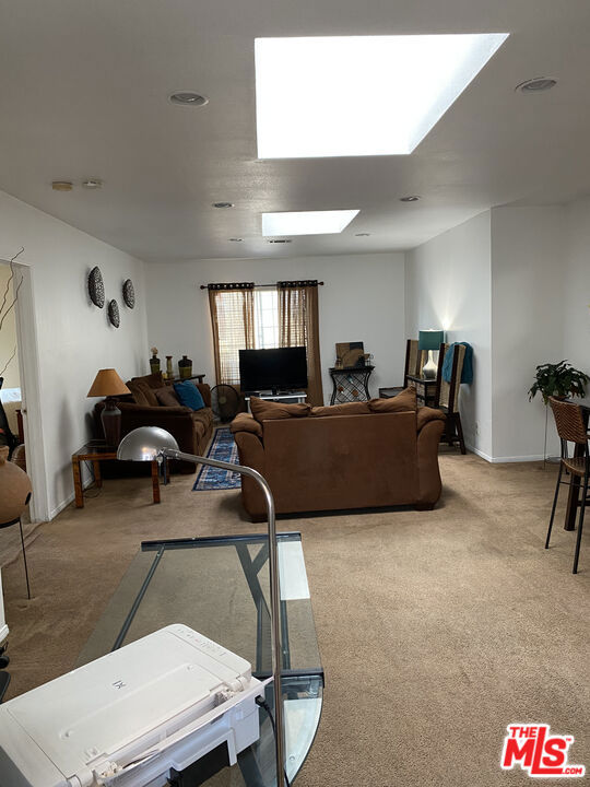 Carpeted living room at 2643 S Spaulding Avenue, with brown sofas facing a TV, a glass coffee table, and large ceiling skylights.