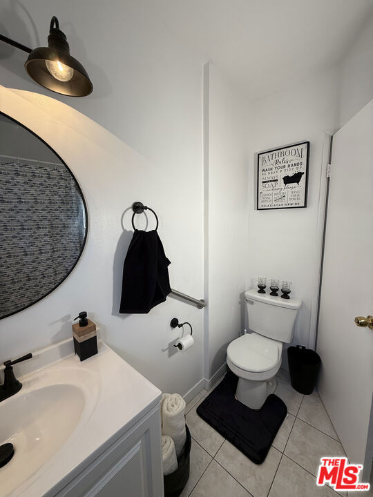 Compact bathroom at 2643 S Spaulding Avenue with a white vanity, round mirror, toilet, and black fixtures.