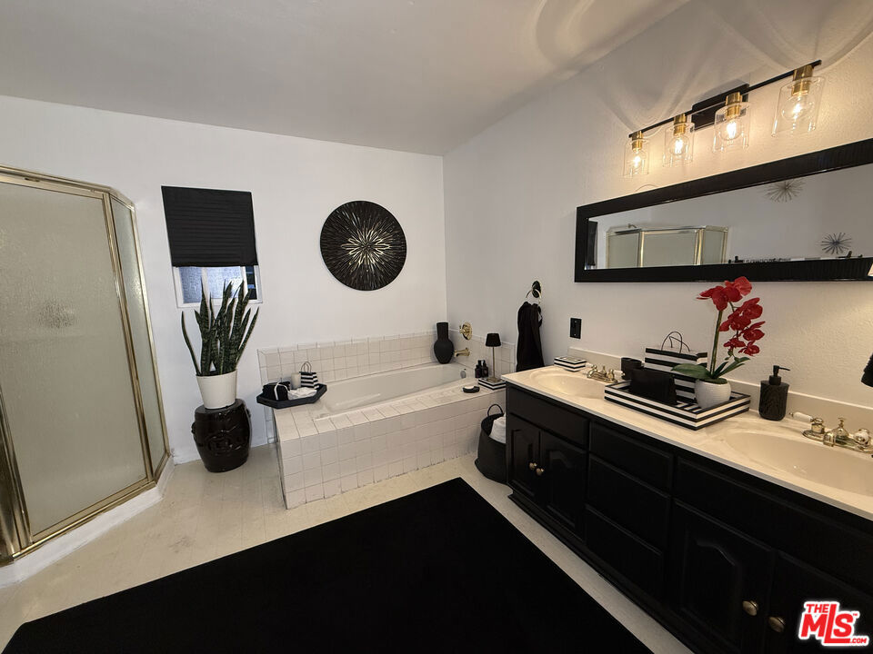 Bathroom at 2643 S Spaulding Avenue with a frosted-glass shower, tiled soaking tub, black vanity, and orchids.