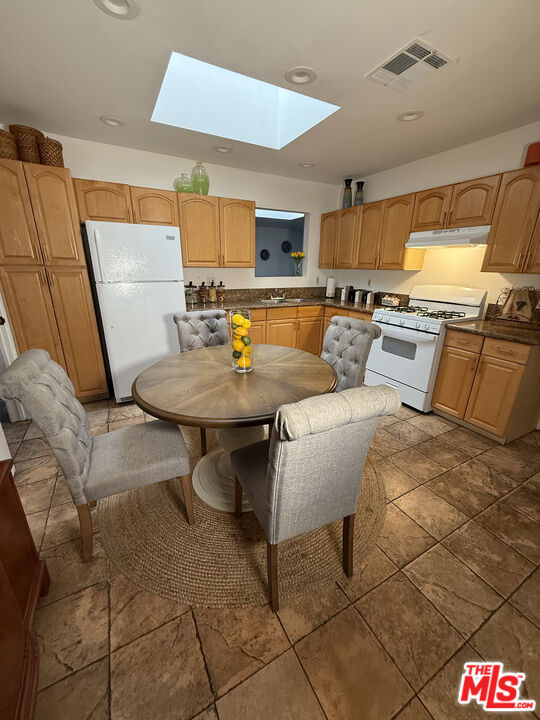 Kitchen at 2643 S Spaulding Avenue with oak cabinets, white appliances, skylight, and a round dining table surrounded by upholstered chairs.