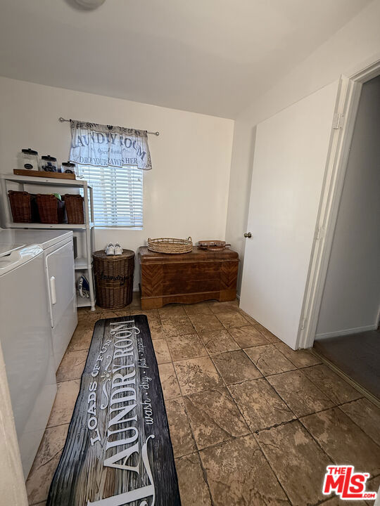 Laundry room at 2643 S Spaulding Avenue with a washer and dryer, window with blinds, wicker hamper, wooden chest, and stone-look tile floor.