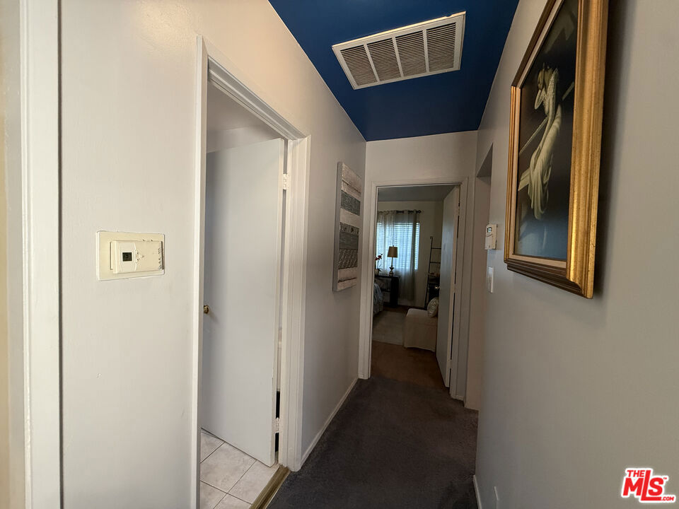 Hallway with carpeted flooring, white walls, a blue ceiling, and a doorway opening to a tiled room at 2643 S Spaulding Avenue.