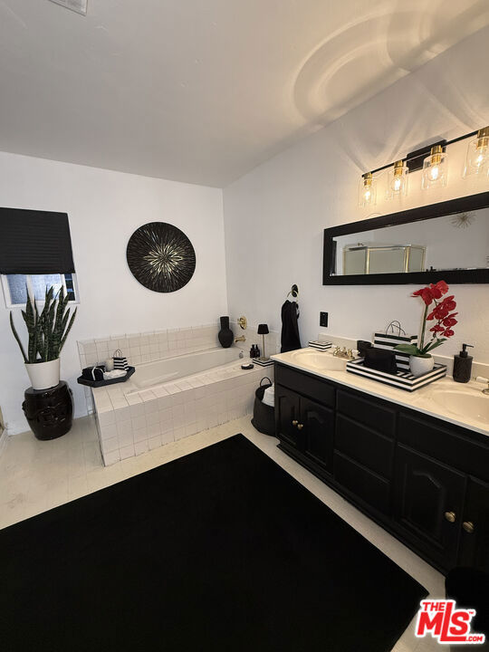Bathroom at 2643 S Spaulding Avenue with a white tiled soaking tub, black vanity and countertop, large mirror, and red orchids.