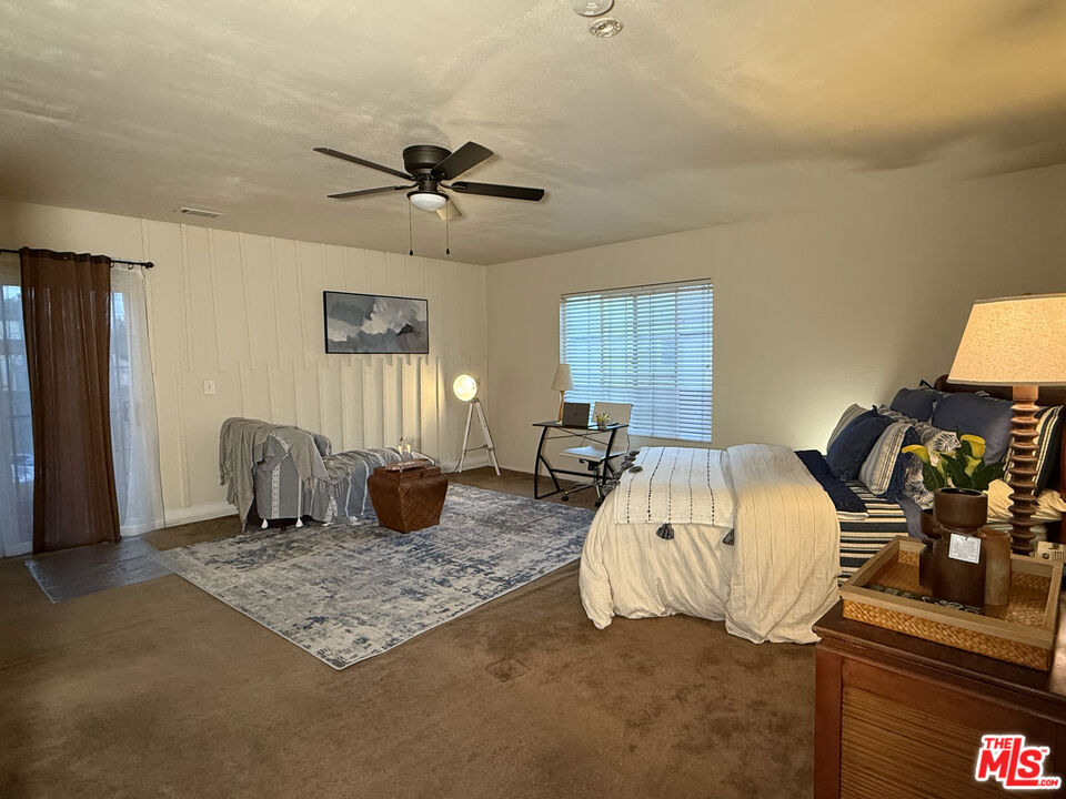 Spacious bedroom at 2643 S Spaulding Avenue with a queen bed, sitting area, desk, ceiling fan, and windows with blinds.