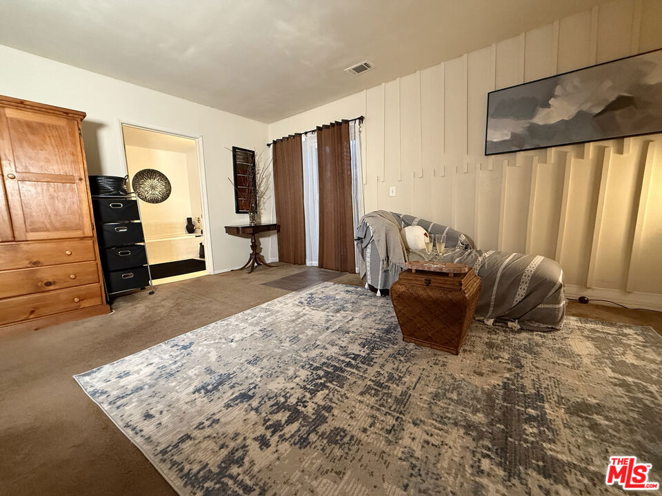Bedroom at 2643 S Spaulding Avenue with a gray upholstered bed, patterned area rug, wooden dresser, and curtained window.