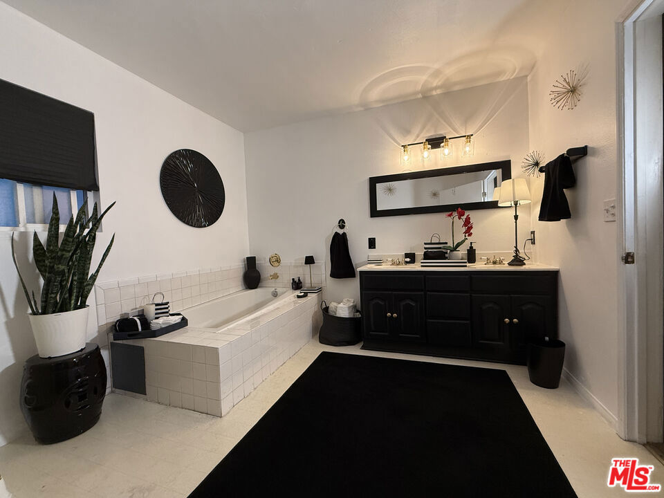 Bathroom at 2643 S Spaulding Avenue with a built-in tiled soaking tub, black vanity, large mirror, and black floor rug.