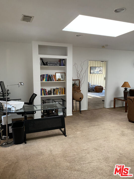 Carpeted office or sitting room at 2643 S Spaulding Avenue with built-in bookshelves, a desk and chairs, and a doorway to a bedroom.
