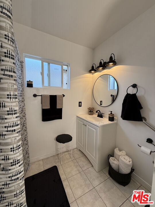 Bathroom at 2643 S Spaulding Avenue with a white vanity, round mirror, tiled floor, patterned shower curtain, and window.