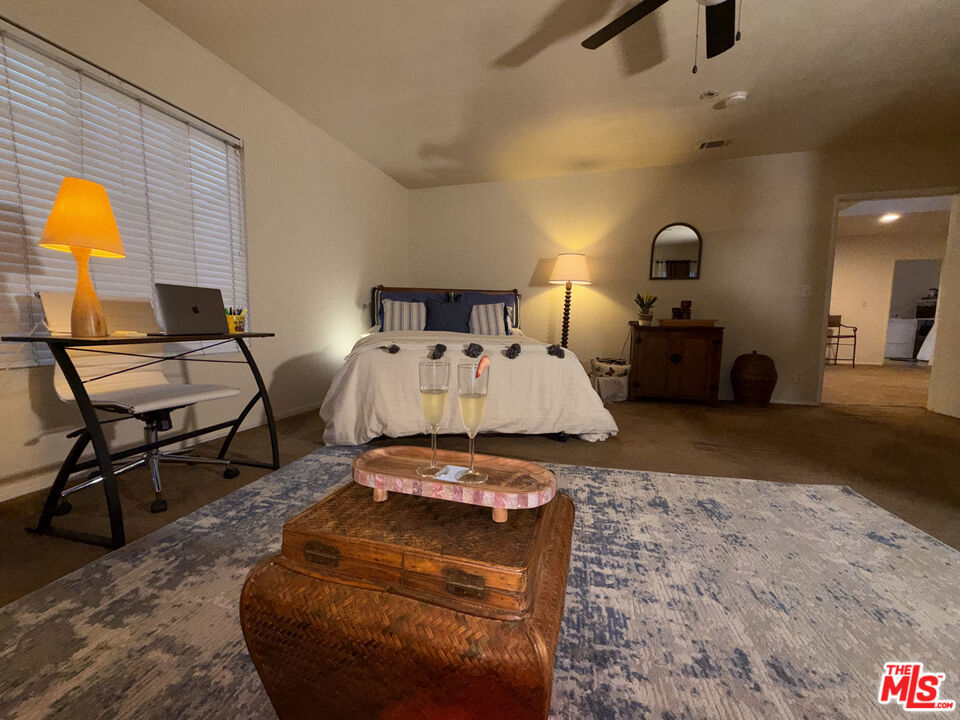 Bedroom at 2643 S Spaulding Avenue with a blue-and-white rug, wooden chest, queen bed, desk by the window, and open doorway to an adjoining room.