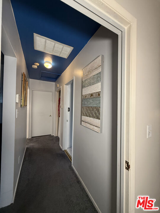 Hallway with dark carpet, gray walls, a navy blue ceiling, and abstract wall art.