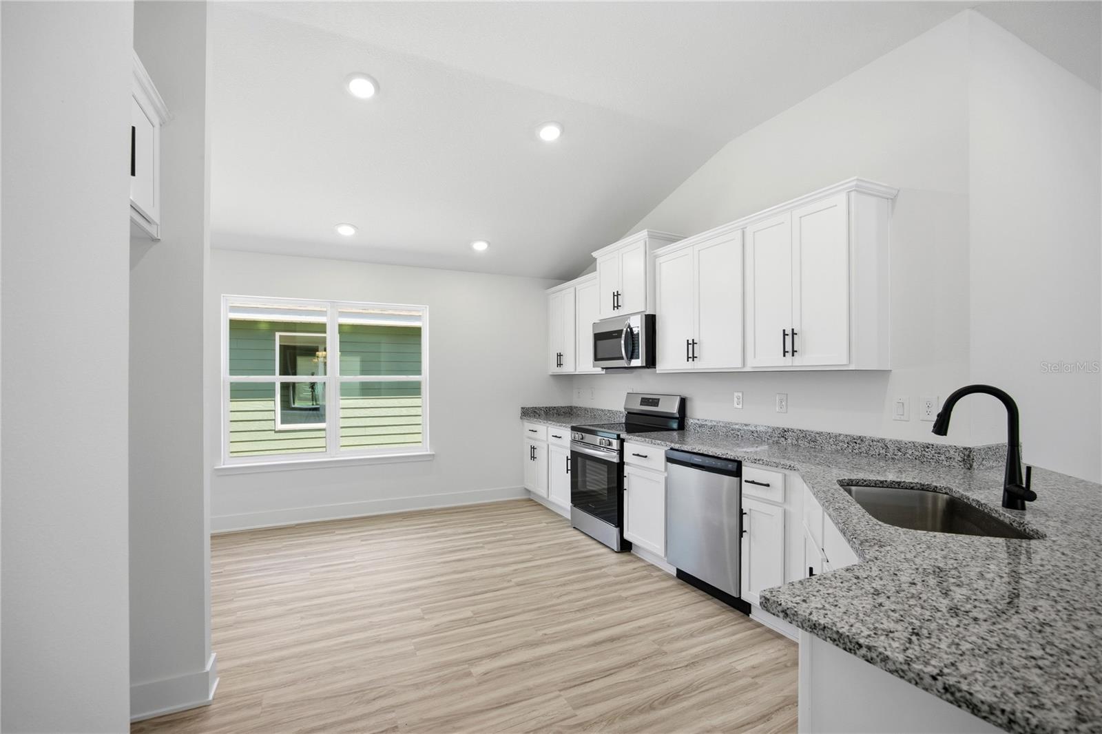 Modern kitchen with white cabinetry, granite countertops, and light wood-look flooring