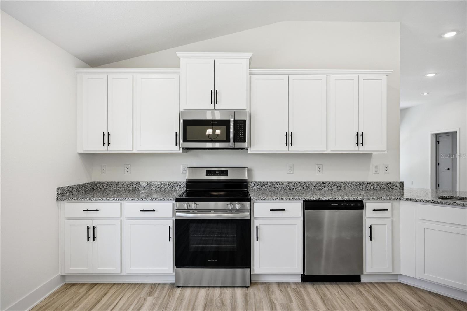 A modern kitchen featuring white shaker-style cabinets, granite countertops, and stainless steel appliances
