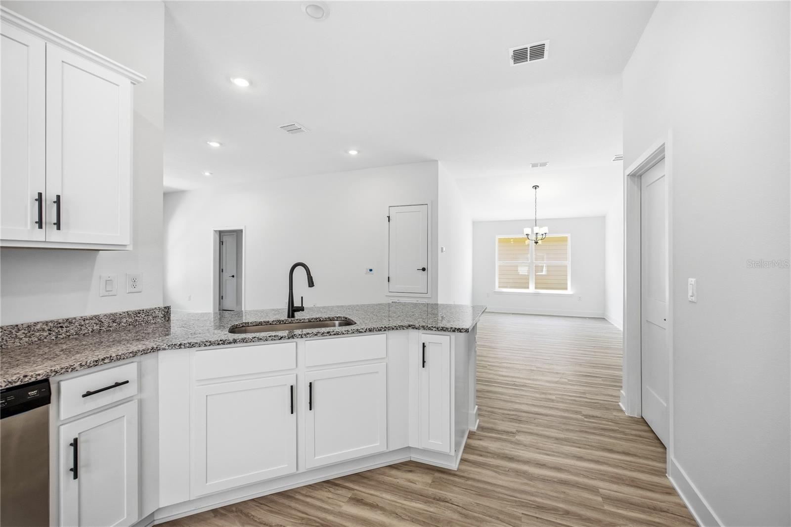 A bright, modern white kitchen with granite countertops and an open view into the dining area.