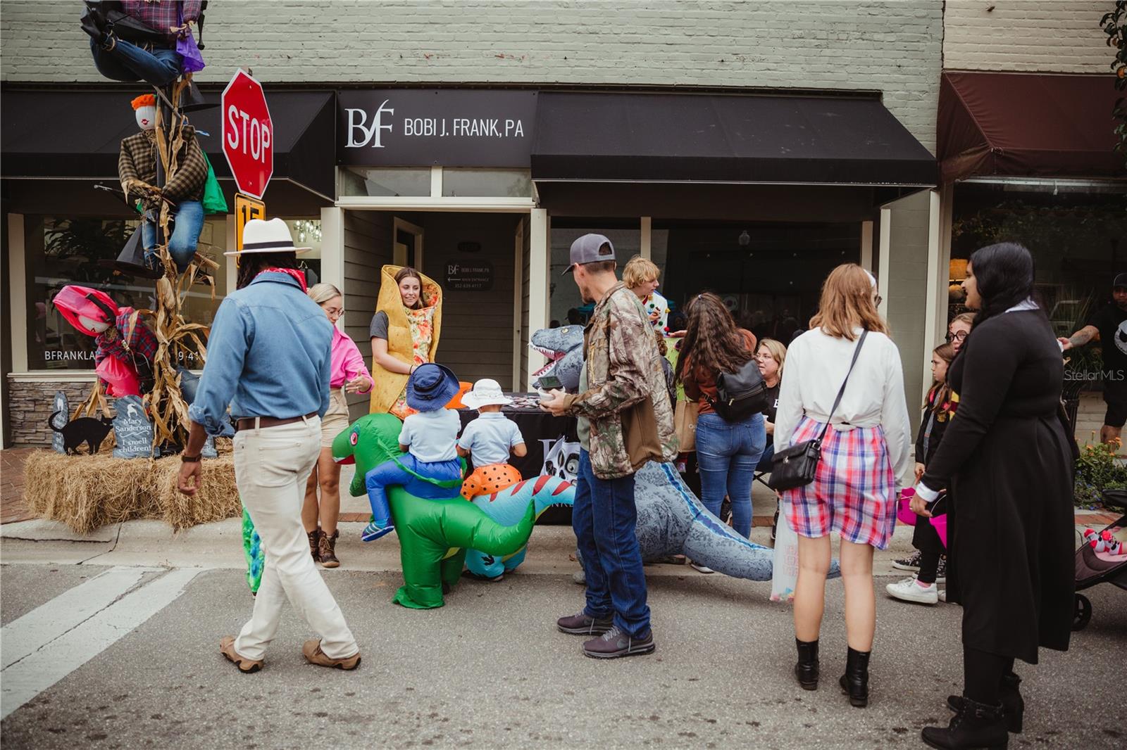 A street scene showing people gathered for a community Halloween event in front of a business called Bobi J. Frank, P.A.