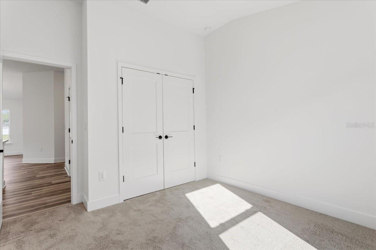A bedroom corner featuring white walls, gray carpet, and double closet doors.