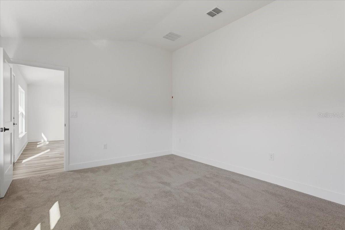 An empty bedroom with neutral carpet and white walls, looking toward an open doorway.