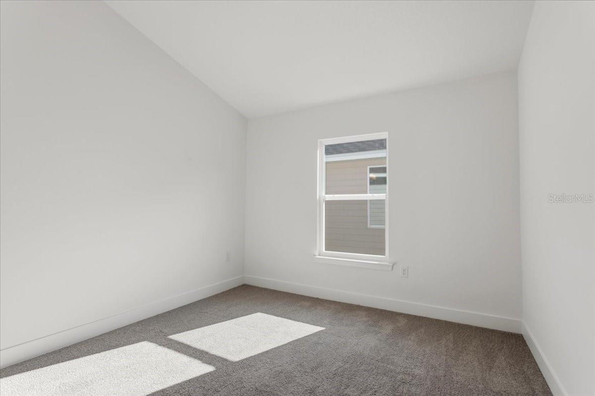 An empty bedroom with white walls and grey carpeting in a new construction home