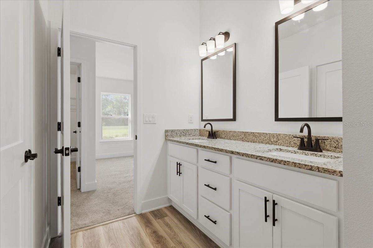 A clean, modern bathroom with a double vanity featuring white cabinets, granite countertops, and black faucets.