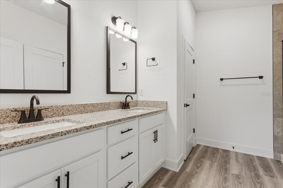A modern bathroom featuring a white vanity with granite countertops, double sinks, dark faucets, and rectangular mirrors.