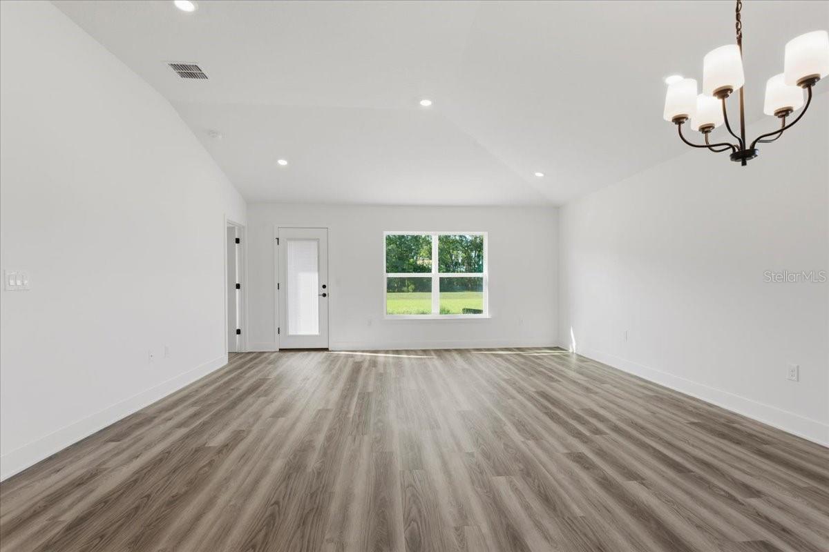 A wide shot of a modern, empty living room with white walls and grey wood-look flooring.