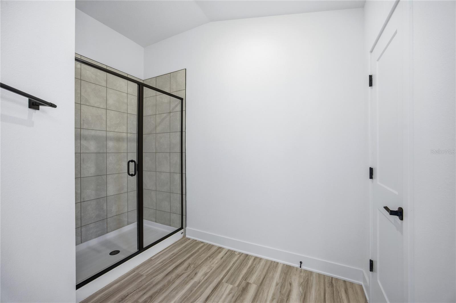 A modern bathroom shower stall with black hardware and tiled walls.