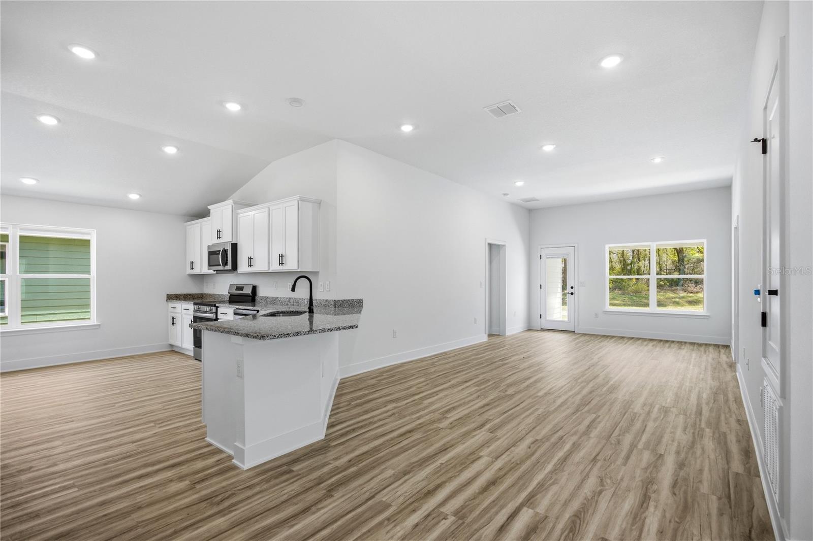 An open-concept kitchen and living area with white cabinets, granite countertops, and light wood-look flooring.