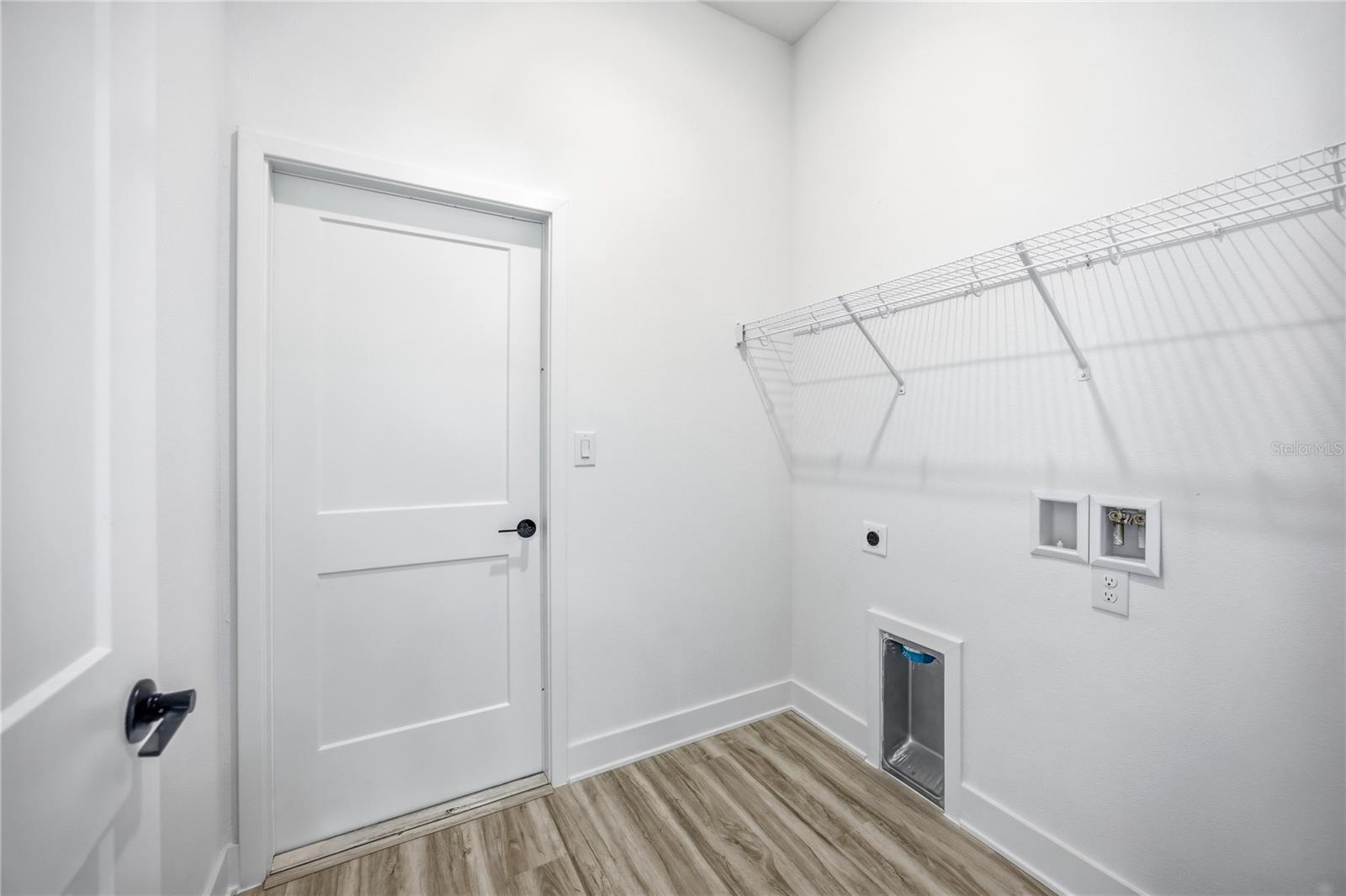 An empty laundry room with white walls, wire shelving, and wood-look flooring