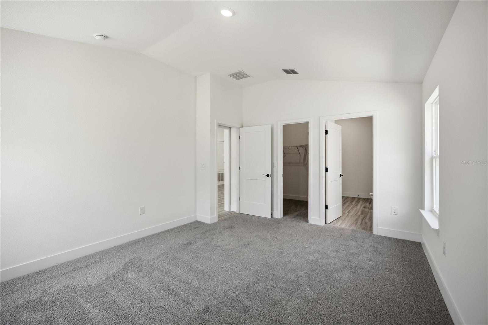 A vacant bedroom with neutral grey carpet and white walls featuring closet and bathroom doors