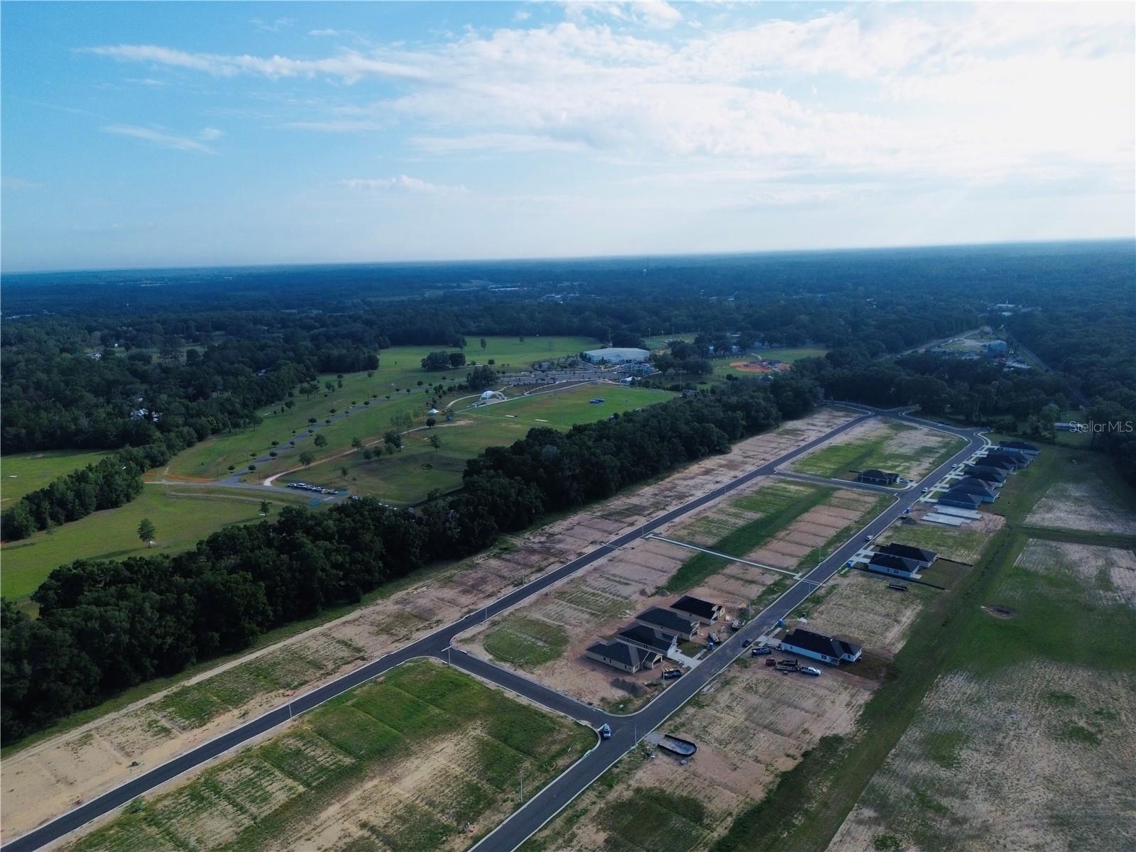 An aerial view of a new housing development under construction with paved roads and a large field in the background