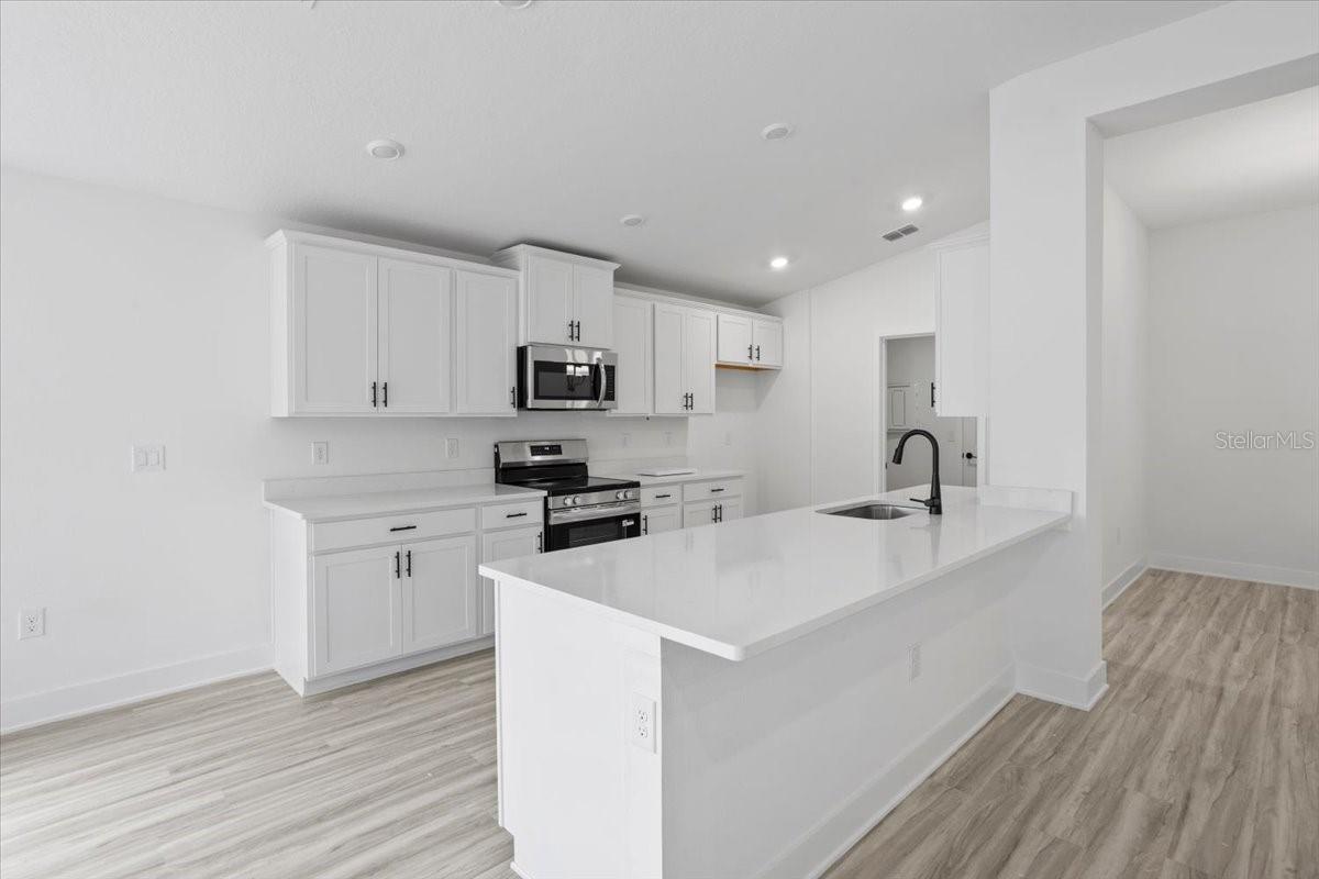 A bright, modern kitchen with white cabinetry, a large kitchen island with sink, and light wood-tone flooring.