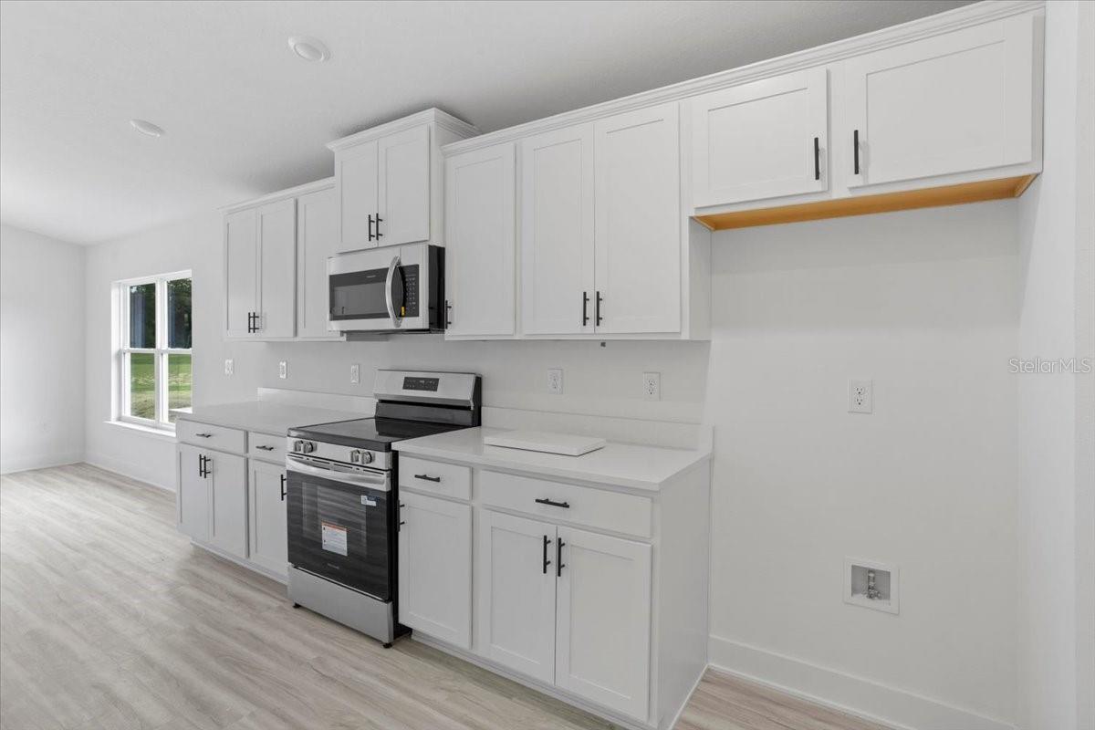 A clean, modern kitchen featuring white shaker cabinets, white countertops, and stainless steel appliances including a range and microwave.