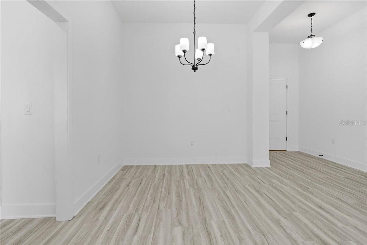 An empty dining room with white walls, light wood-look flooring, and a chandelier.