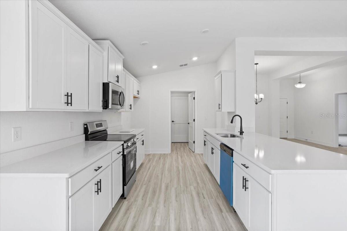 A modern, bright, all-white kitchen with white cabinets, light wood-look flooring, stainless steel appliances, and a quartz countertop island.