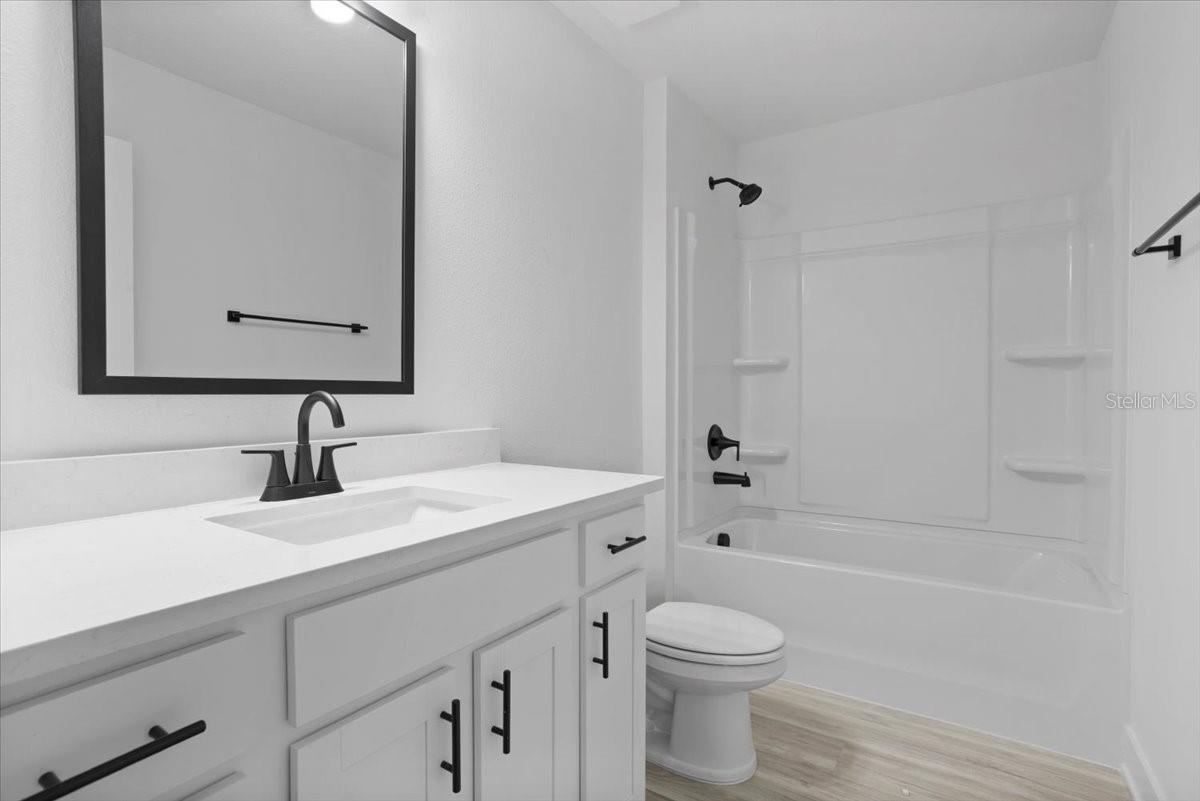 A modern white bathroom with a black framed mirror, black faucet, and a white bathtub shower combination.