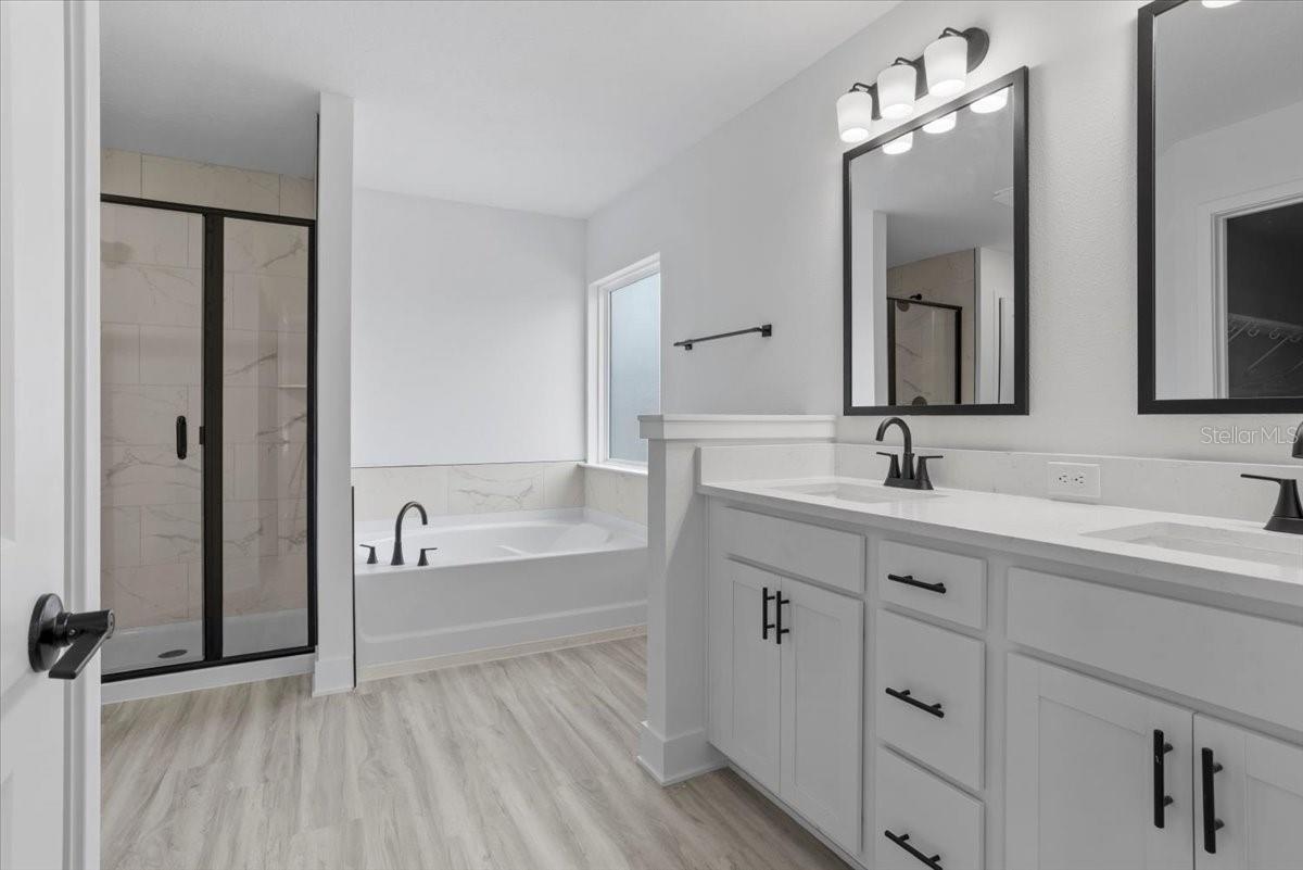 A modern master bathroom with white vanity cabinets, black fixtures, a soaking tub, and a glass-enclosed shower.