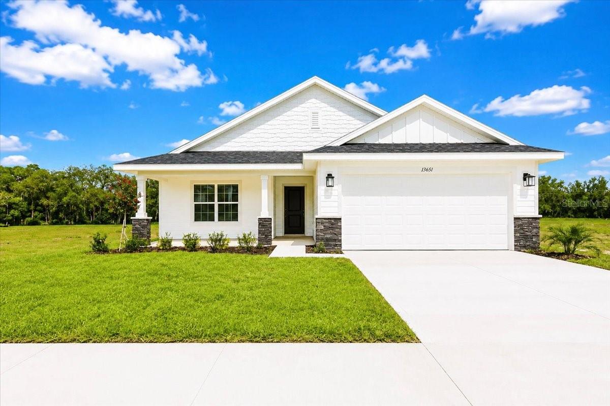Single story white farmhouse style home with attached garage and driveway on a grassy lot under blue sky