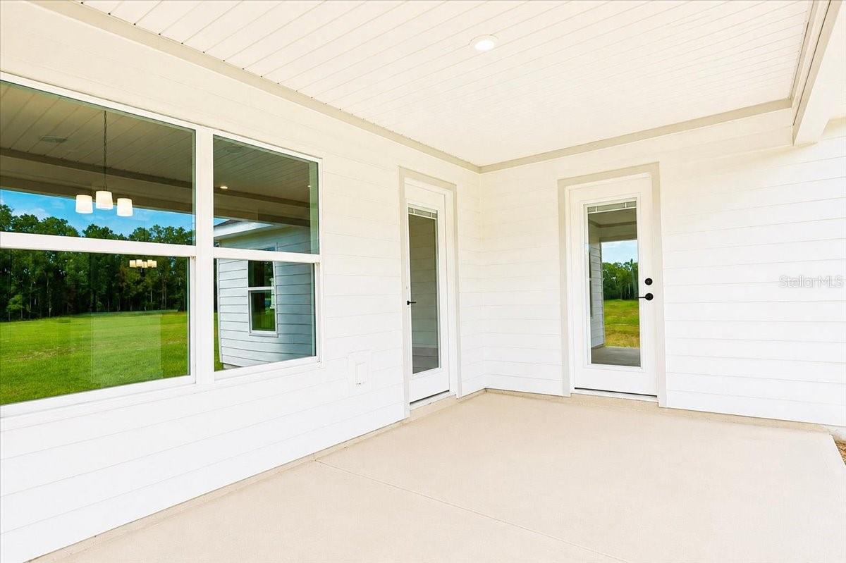 A modern covered patio with white siding and glass doors looking out over a grassy field