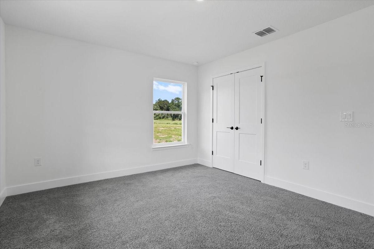 An empty bedroom with white walls, grey carpet, and a white double door closet.