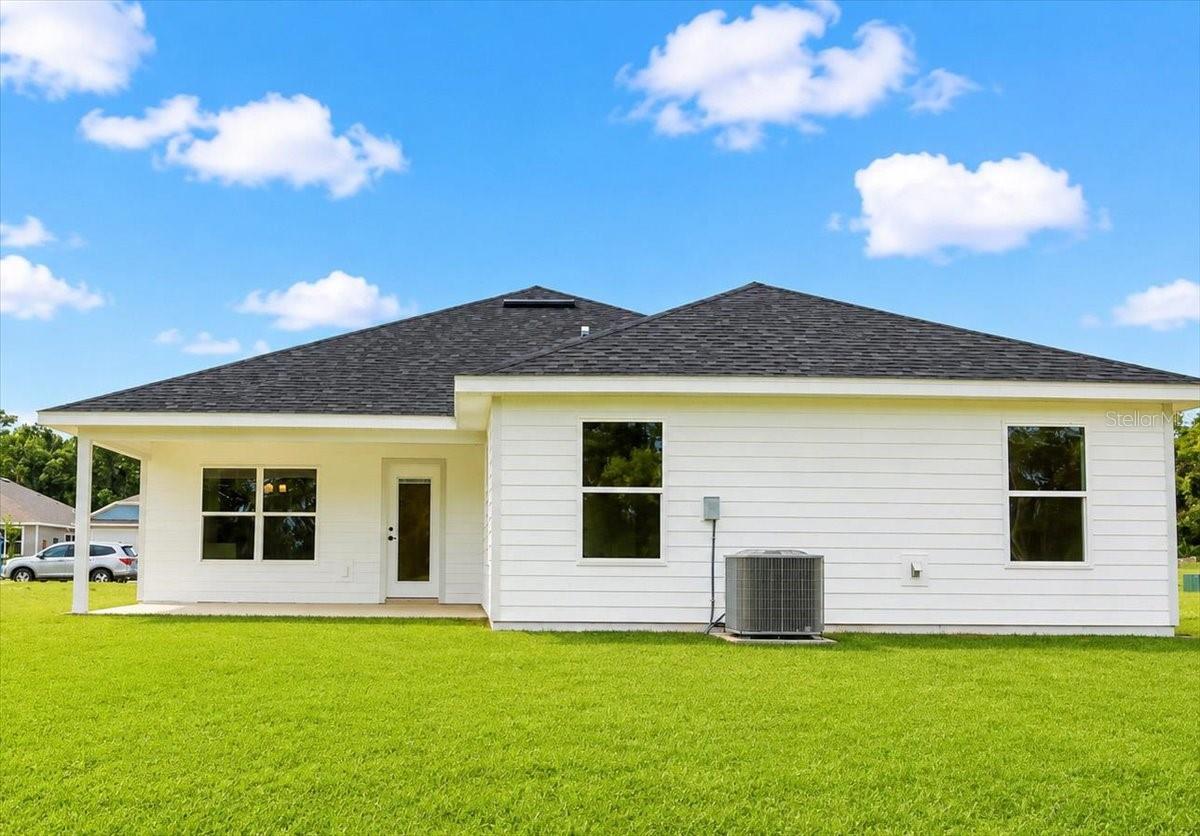 Rear exterior view of a white single-story house with a lawn and dark shingle roof