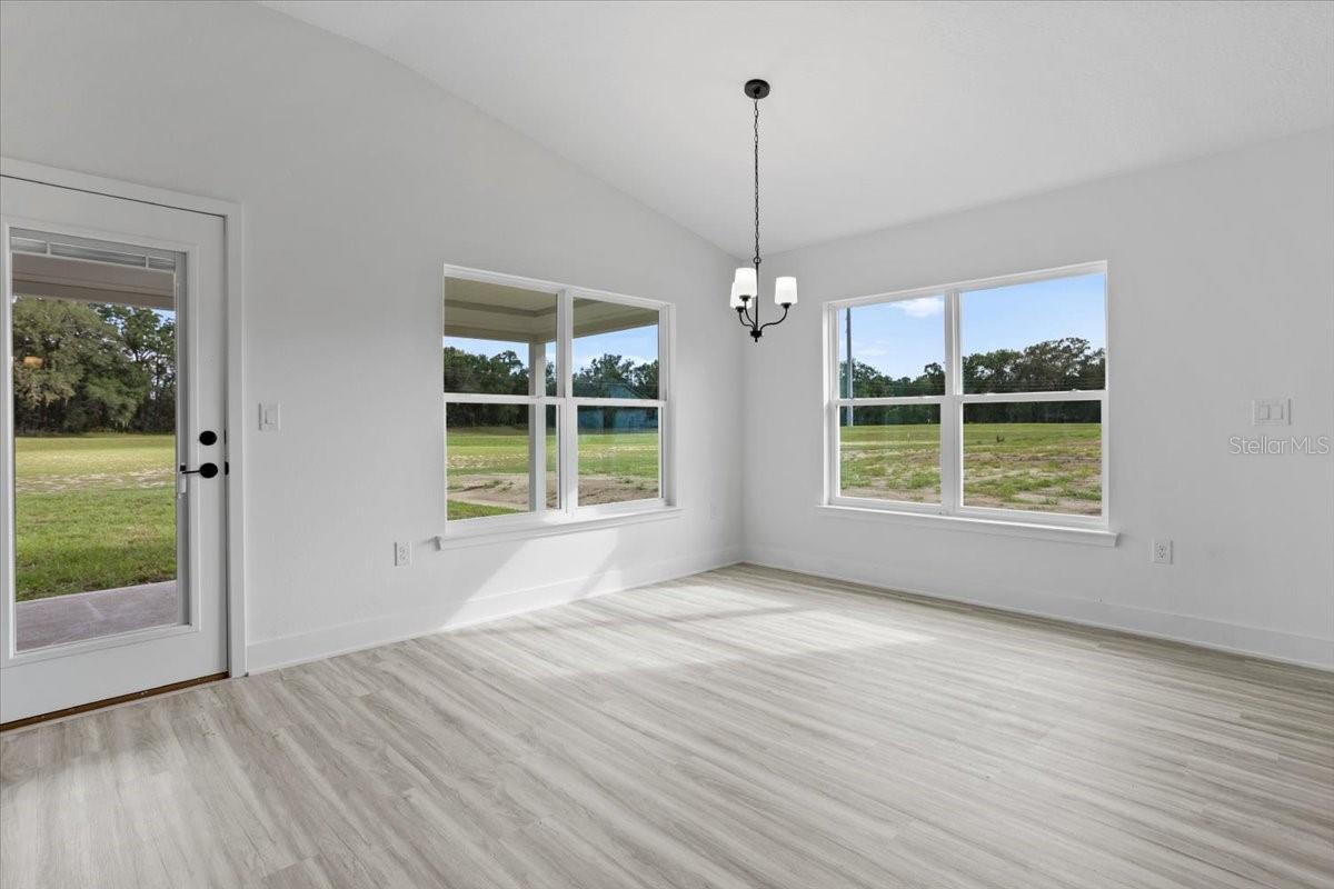 Bright dining area with white walls, wood-look flooring, a modern chandelier, and large windows with exterior view.