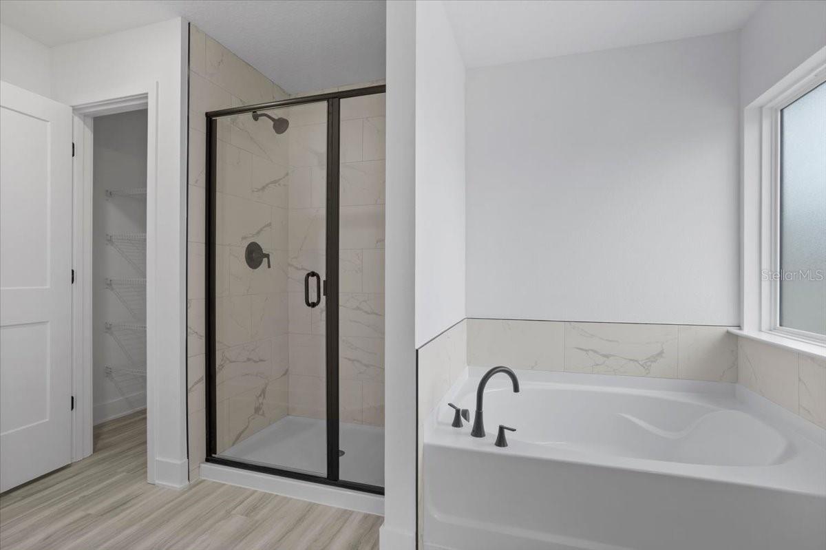 A modern master bathroom featuring a glass-enclosed shower with black fixtures and a white soaking tub below a window.