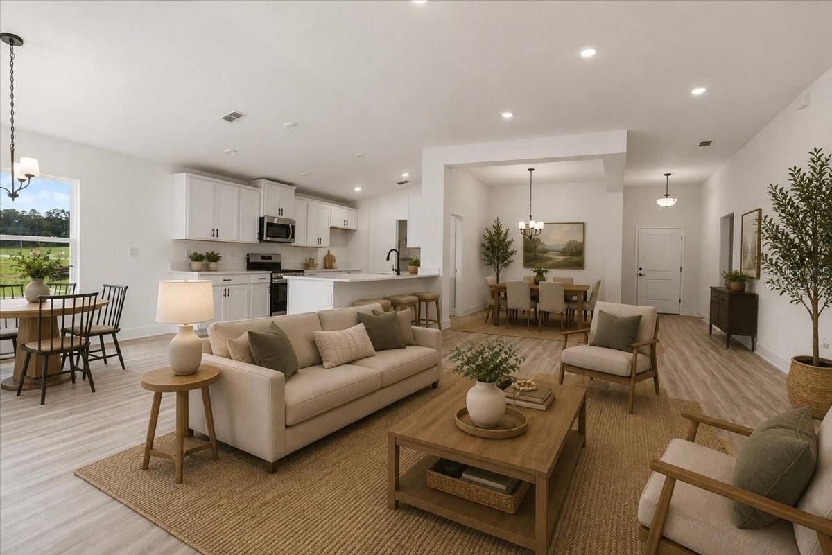 Open floor plan featuring a living room with a beige sofa, wooden coffee table, a dining area in the background, and a modern kitchen with white cabinets.