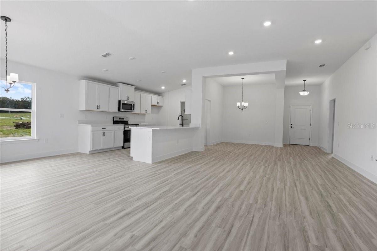 An open-concept kitchen and dining space in a modern home with white cabinets, light wood-look flooring, and neutral walls.