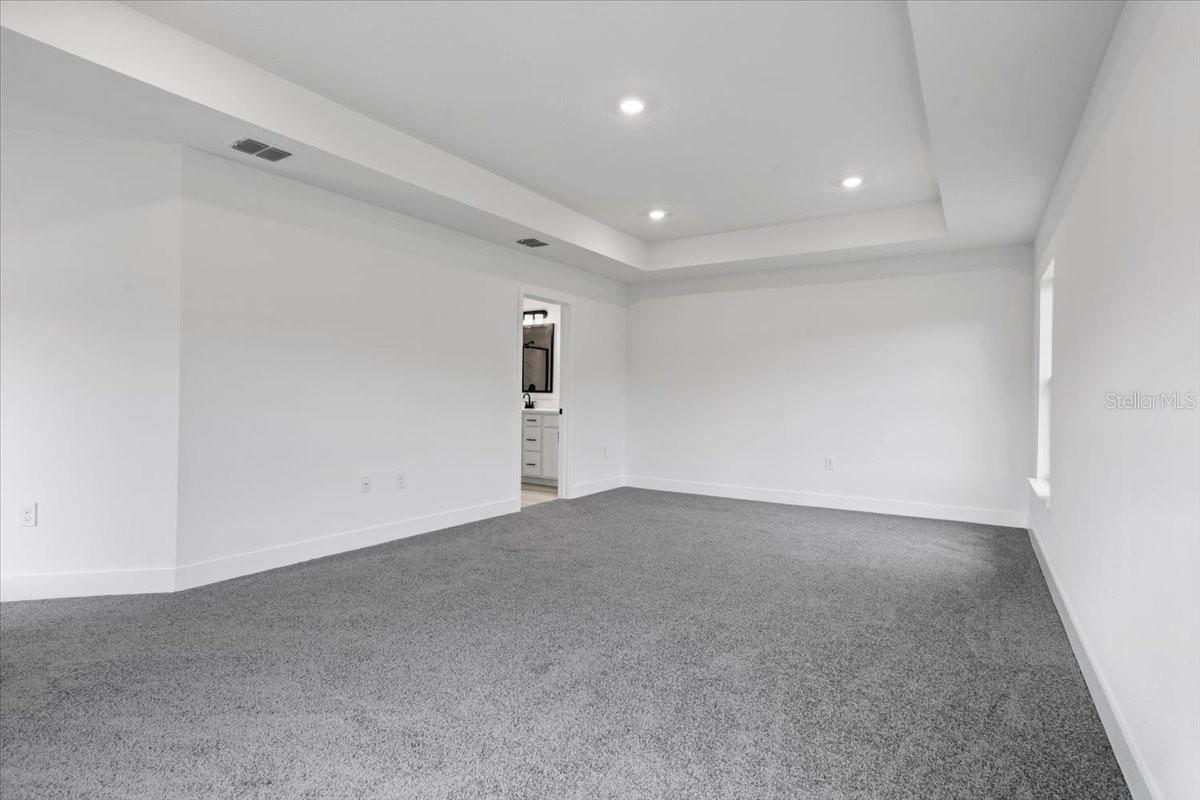 An empty bedroom with gray carpet, white walls, and a recessed ceiling with recessed lighting.