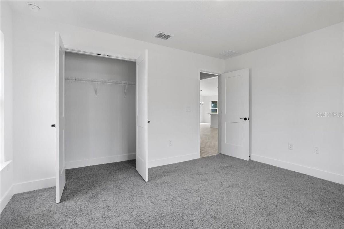 A bright bedroom with white walls, grey carpet, and an open closet door.